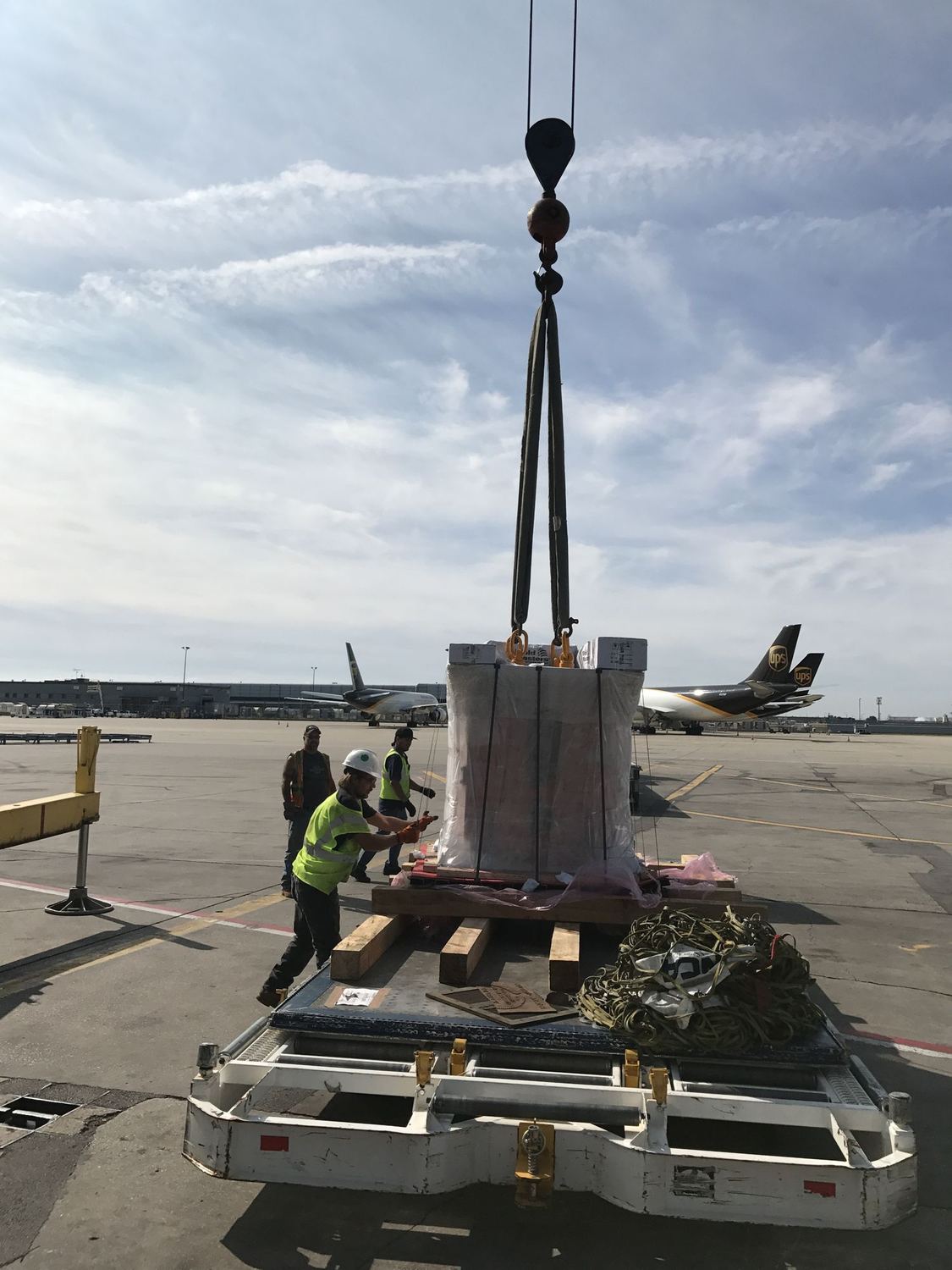 Ground crew loading crated cargo onto a high loader with a crane on the ramp